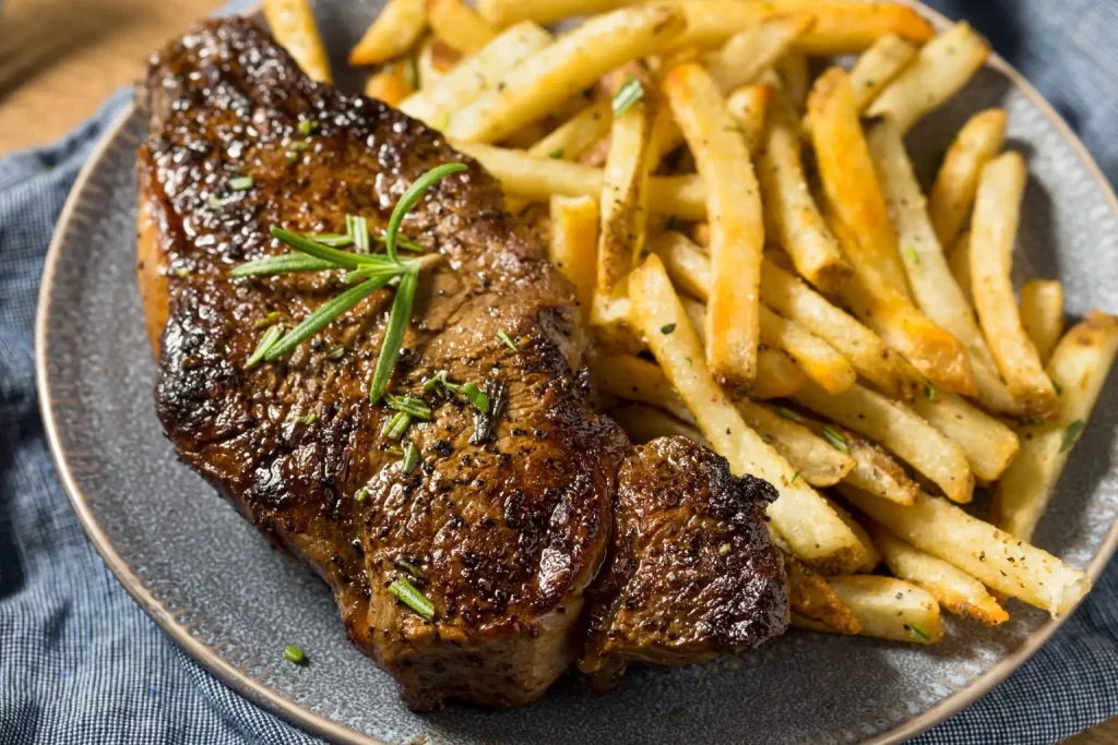 Saftiges Rindersteak mit Rosmarin und knusprigen Pommes auf grauem Teller